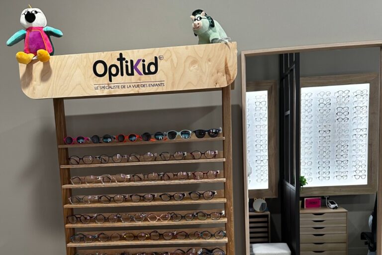 étagère en bois avec logo Optikid sur le dessus et des étagères de lunettes de vue