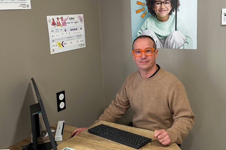 opticien avec des lunettes de vue oranges assis devant son ordinateur