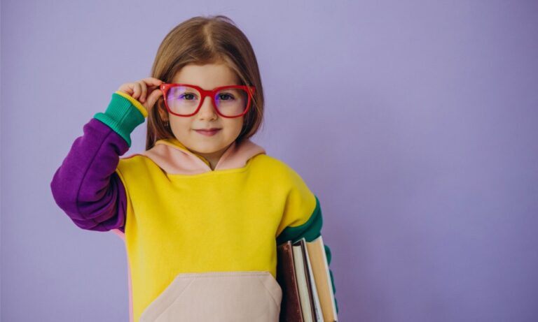 Fille avec un pull jaune, beige et vert qui tient d'une main ses grandes lunettes de vue rouge